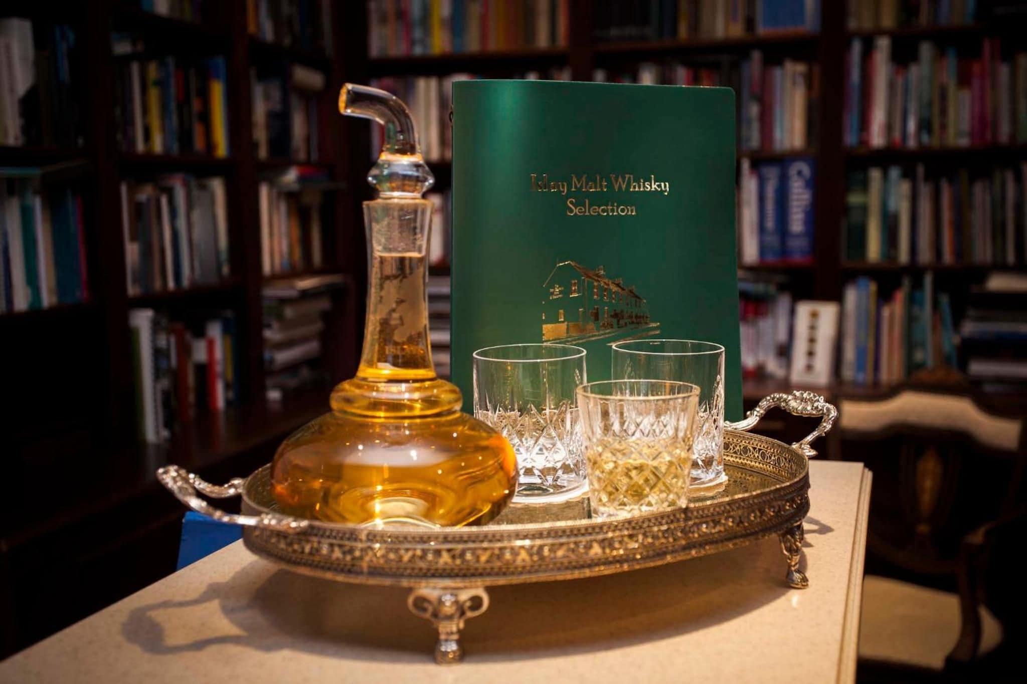 Un decantador, dos vasos y un libro con el título 'Daily Malt Whisky Selection' sobre una bandeja.