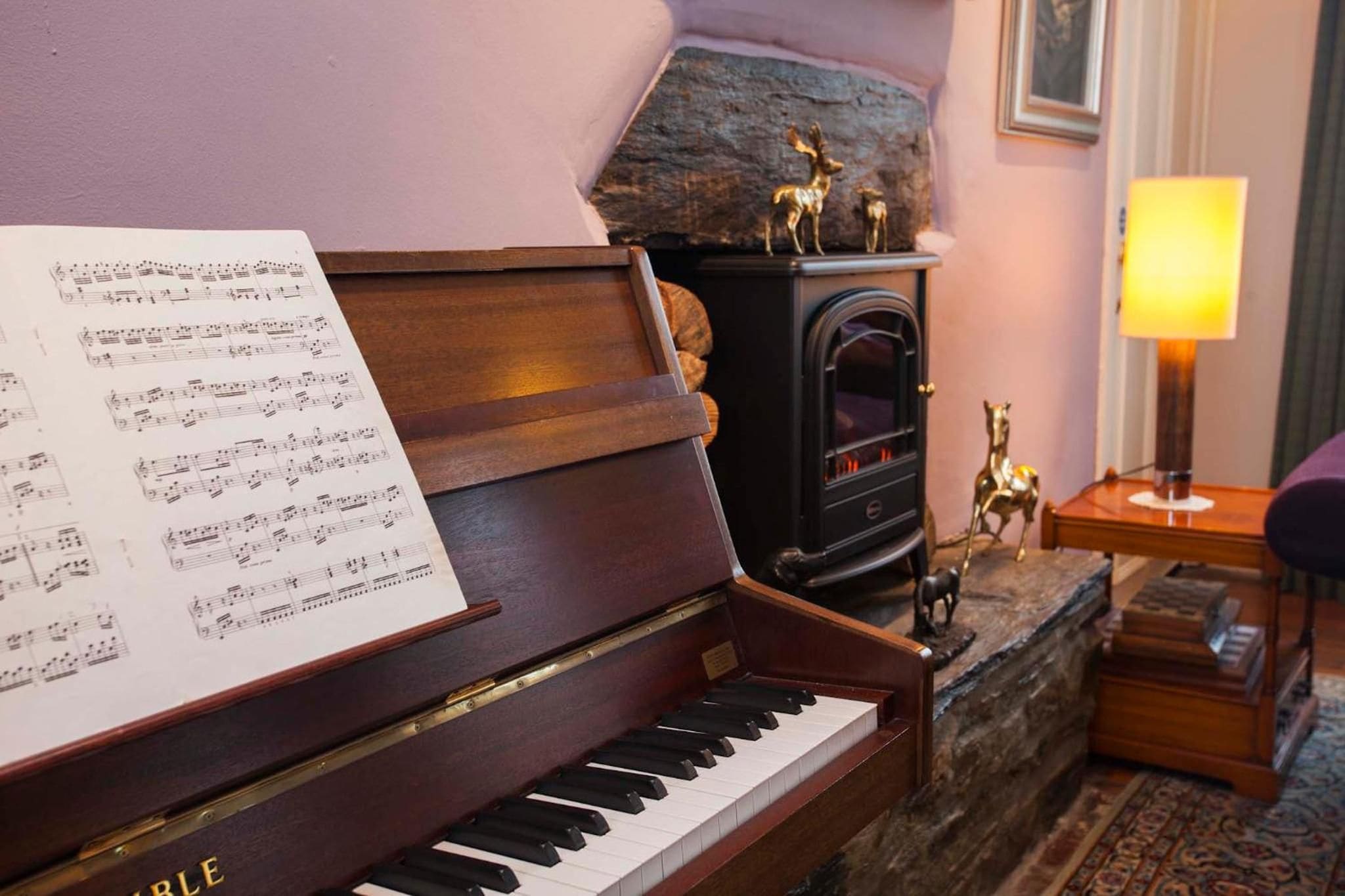 A piano with sheet music, a fireplace with decorative items, and a lamp.