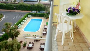 A balcony with a view of a swimming pool, outdoor seating, and a table with flowers. - Residence Villa Gloria (Borgio Verezzi)