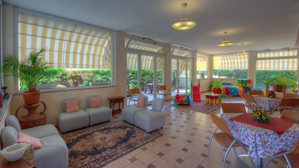 A spacious indoor area with a large window, a sofa set, a dining table with chairs, and a play area with toys. - Residence Villa Gloria (Borgio Verezzi)
