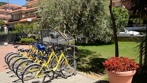 A row of yellow bicycles parked in a designated area, a large potted plant with red flowers, and a building with balconies in the background. - Residence Villa Gloria (Borgio Verezzi)