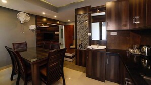 A modern kitchen with dark wood cabinets, a built-in sink, and a dining area with a glass table and wooden chairs. - Ambalath Maple Leaves - Hostel (Chavakkad)