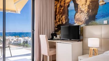 A hotel room with a desk, a television, a lamp, and a bed.