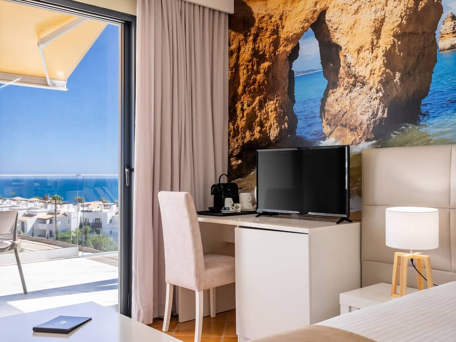A hotel room with a desk, a television, a lamp, and a bed.