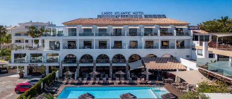 A multi-story hotel with a swimming pool, outdoor seating, and a reception area.