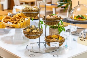 A buffet with various bread options, including cereal and pumpkin bread, displayed on a white table.