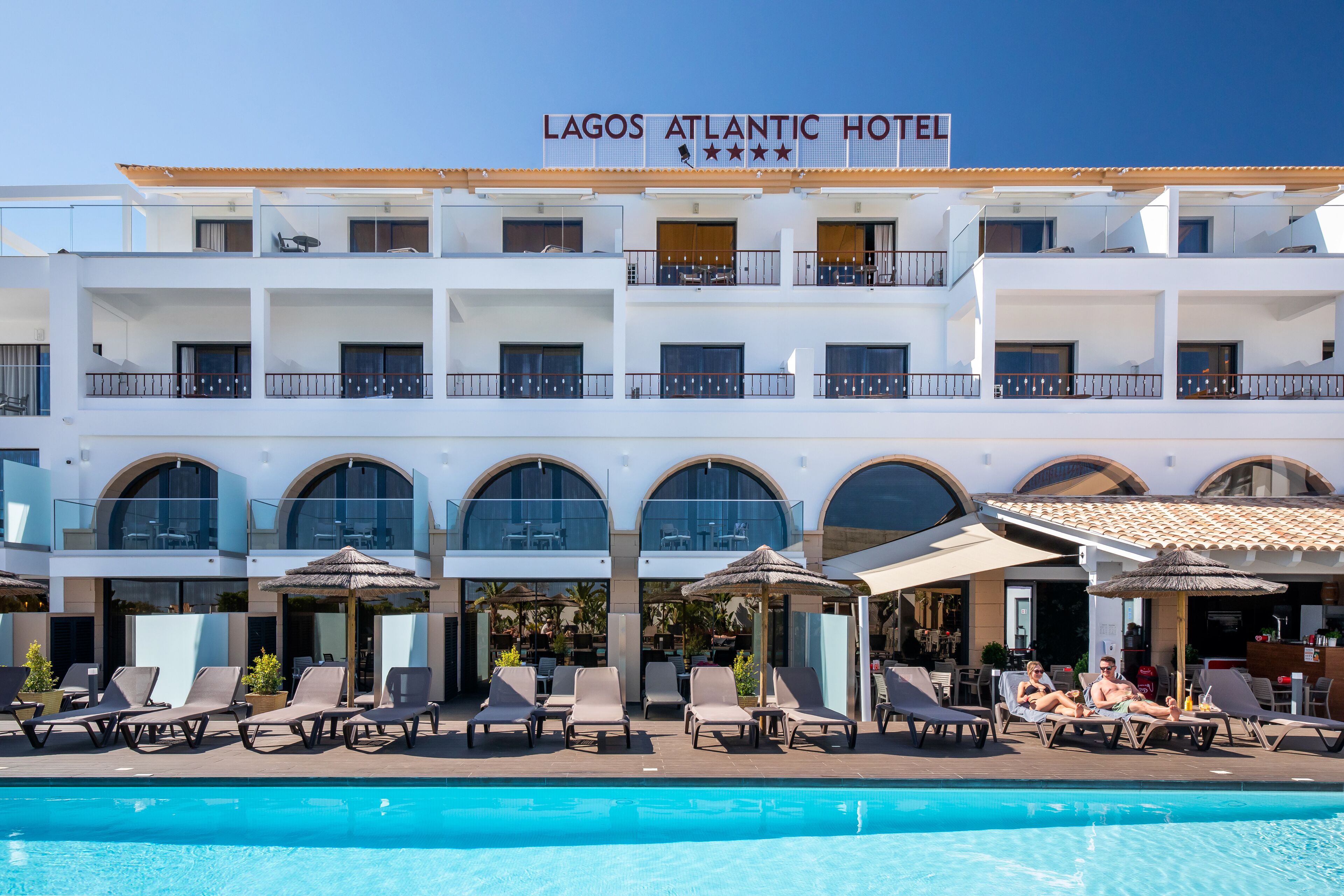 A hotel with a pool area, sun loungers, and umbrellas.