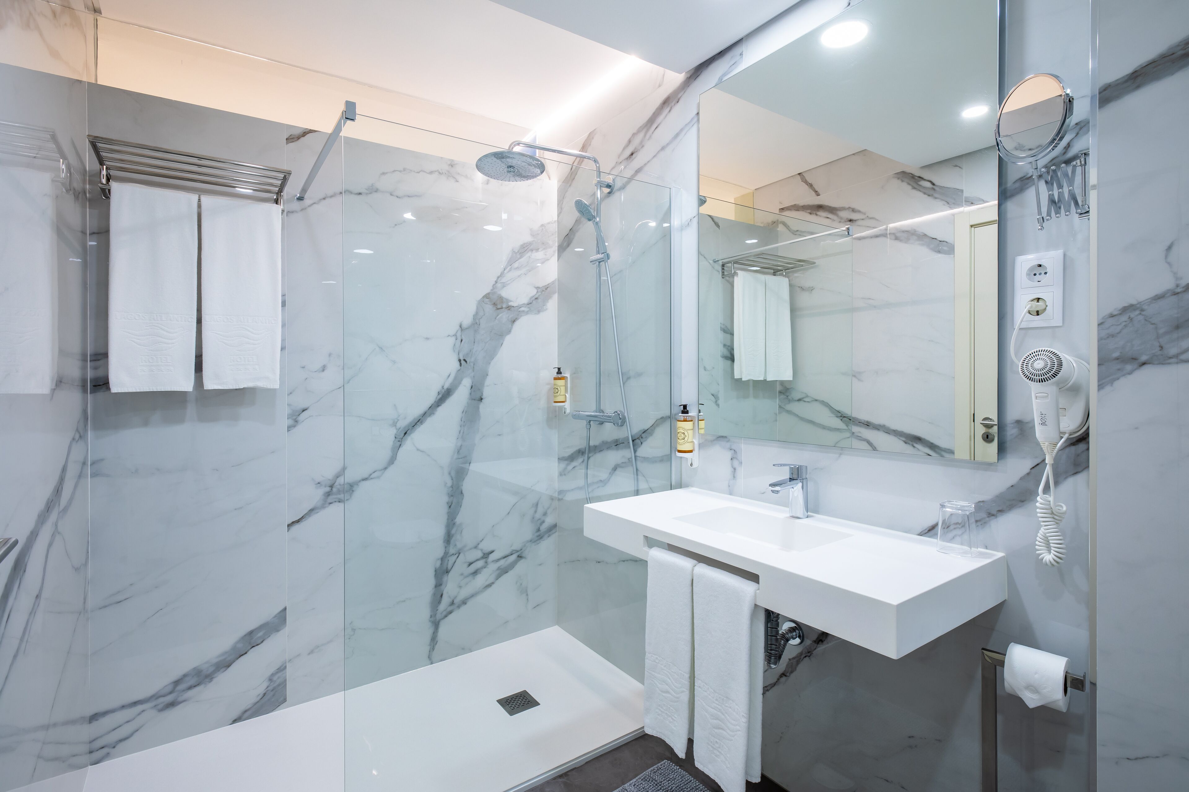 A modern bathroom with a glass-enclosed shower, a white sink, and a marble backsplash.