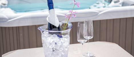 Una mesa con una botella de champán en una copa, cubitos de hielo y dos copas de vino vacías. Se ve una bañera de hidromasaje al fondo.