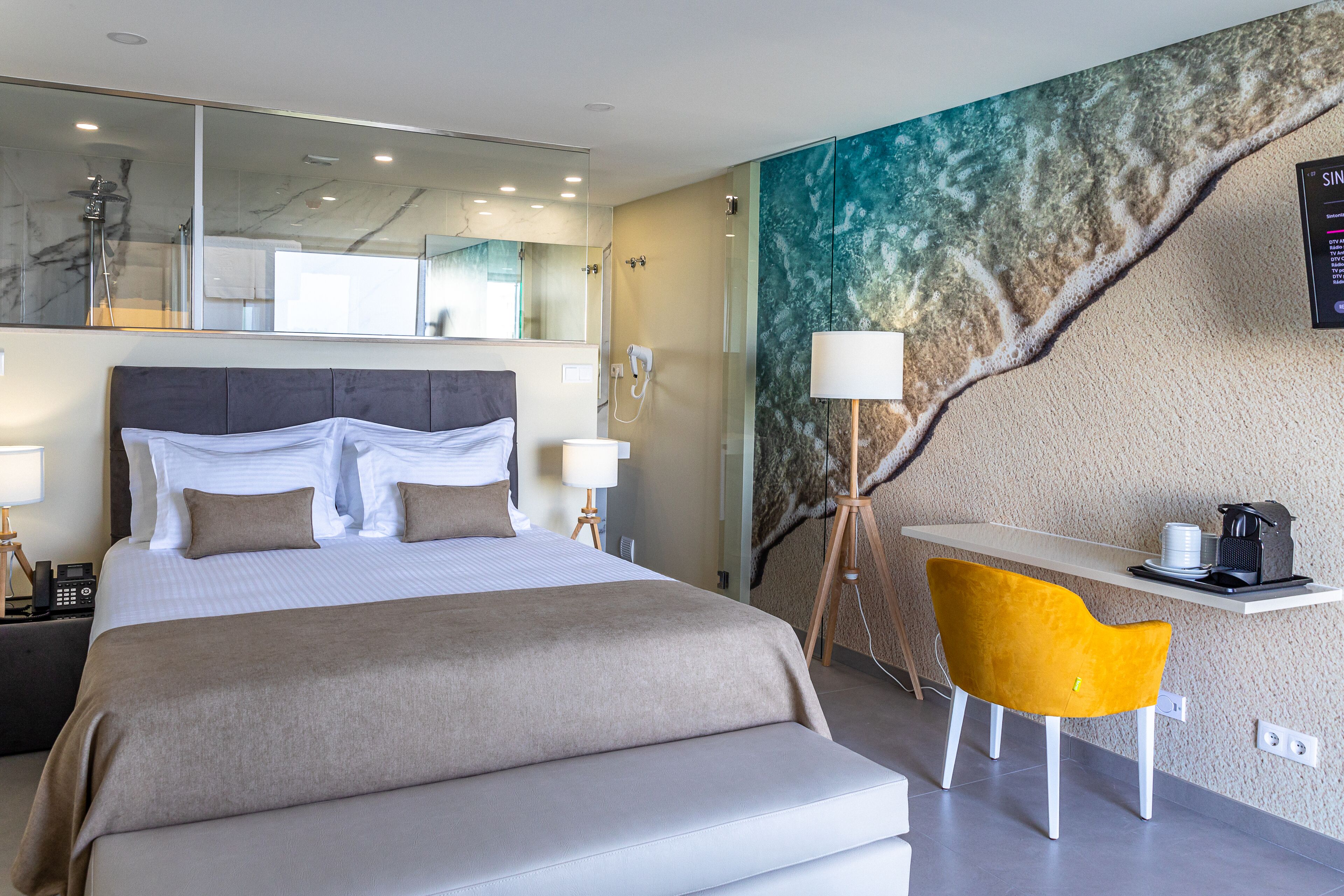 Una camera d'hotel con un letto grande, una scrivania con una sedia, uno specchio ampio e un affresco sulla parete.