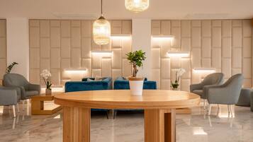 Un vestíbulo moderno con una mesa redonda de madera, sofás azules, sillones grises y una planta en maceta.