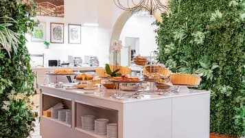 A buffet setup with various food items and baskets, surrounded by greenery and framed artwork on the walls.