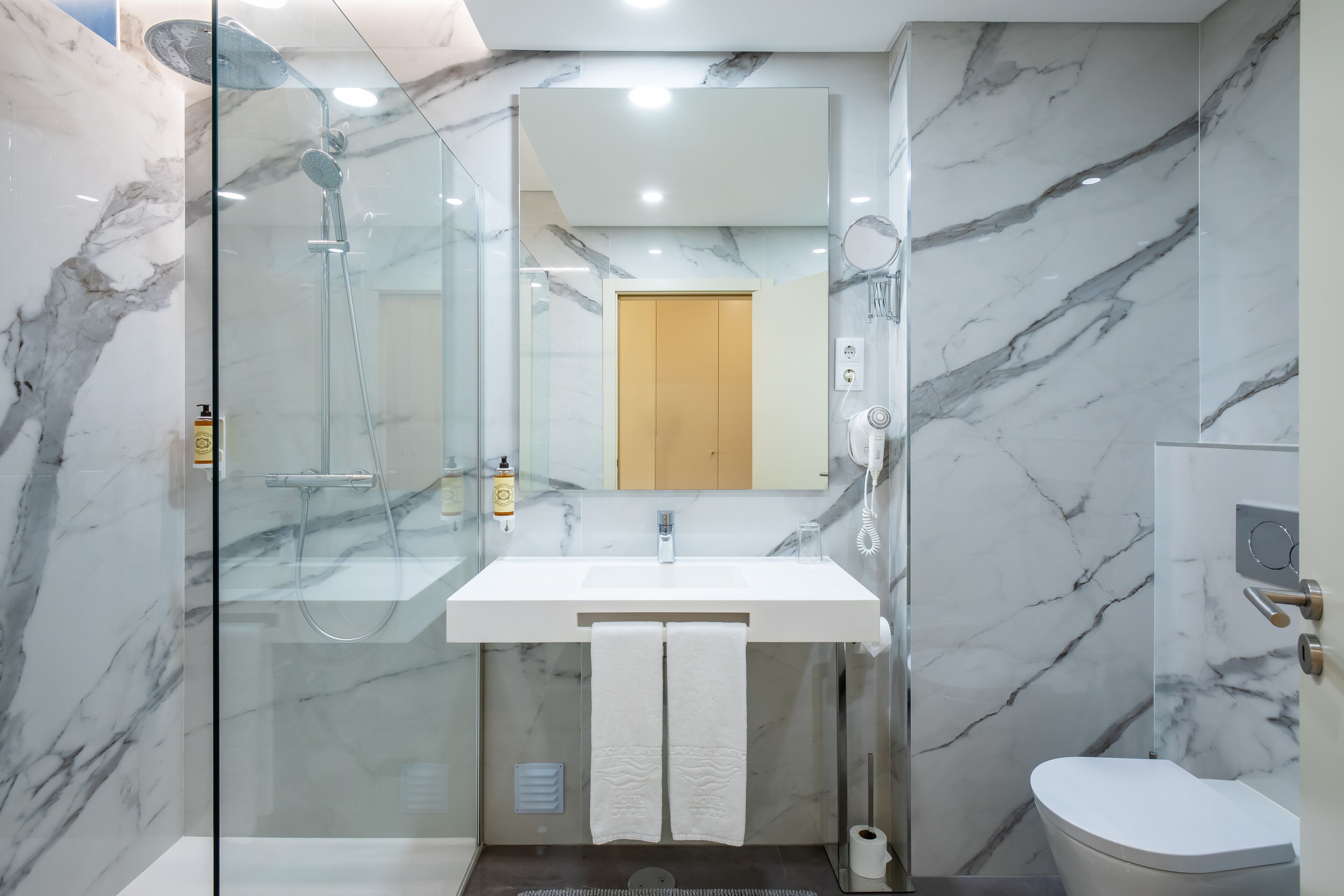 A modern bathroom with a glass-enclosed shower, a marble sink, and a toilet.