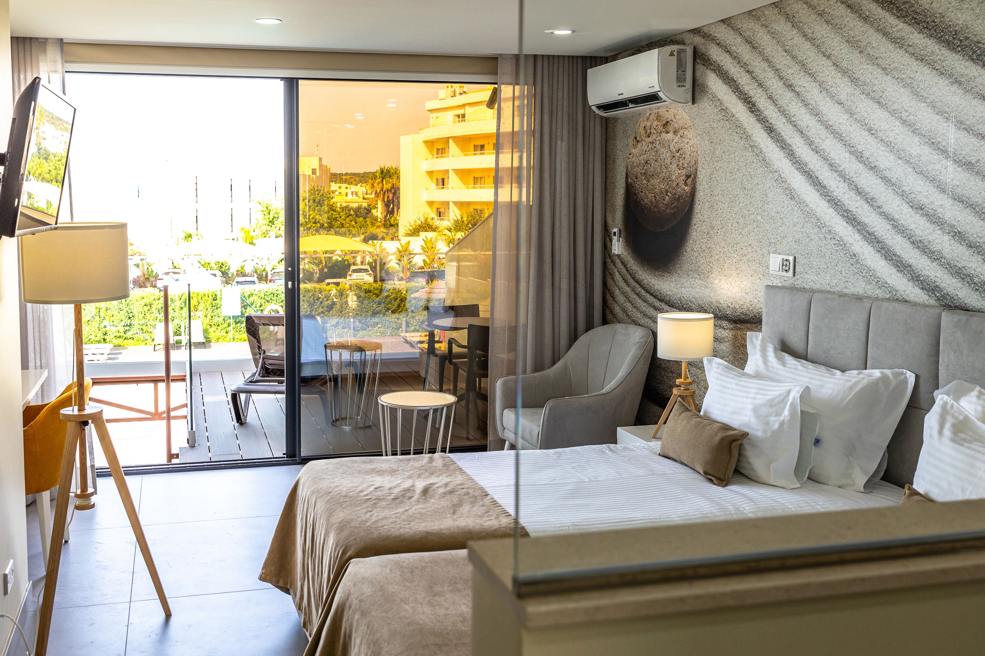 A hotel room with a bed, a chair, a table, and a view of the outside.