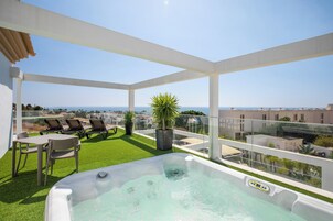 A rooftop terrace with a hot tub, seating area, and a view of the sea.
