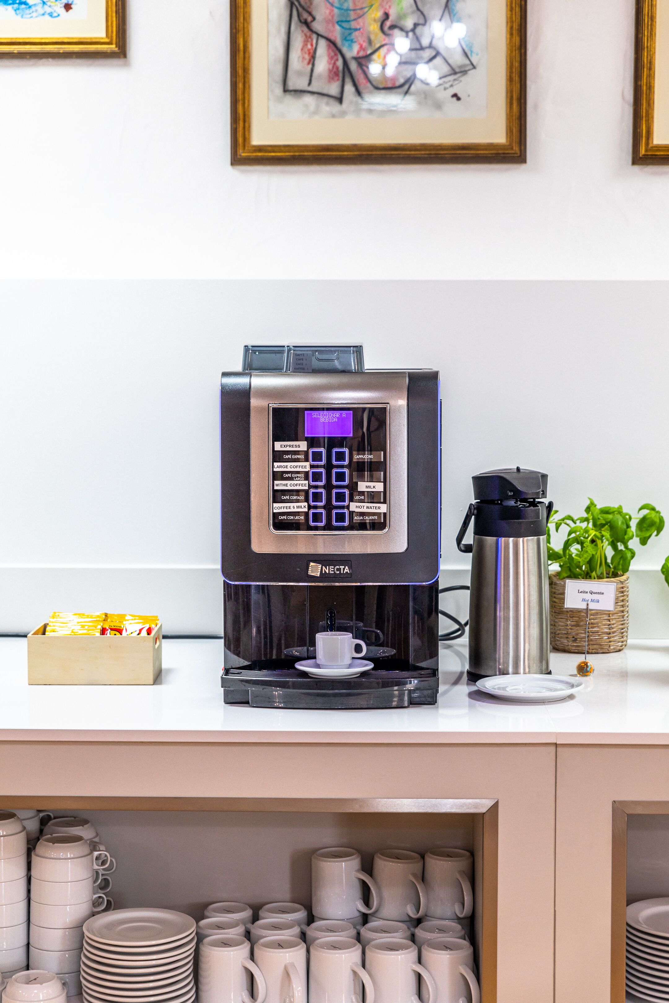 Une machine à café dotée d’un écran numérique, un thermos et un panier rempli de capsules de café, le tout posé sur un comptoir.
