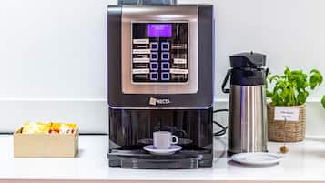 Une machine à café dotée d’un écran numérique, un thermos et un panier rempli de capsules de café, le tout posé sur un comptoir.