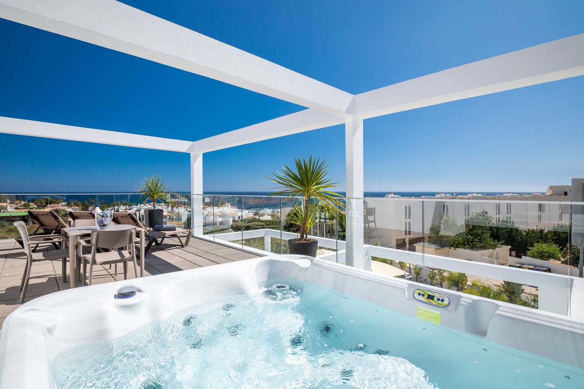 A rooftop terrace with a hot tub, seating area, and a view of the ocean.