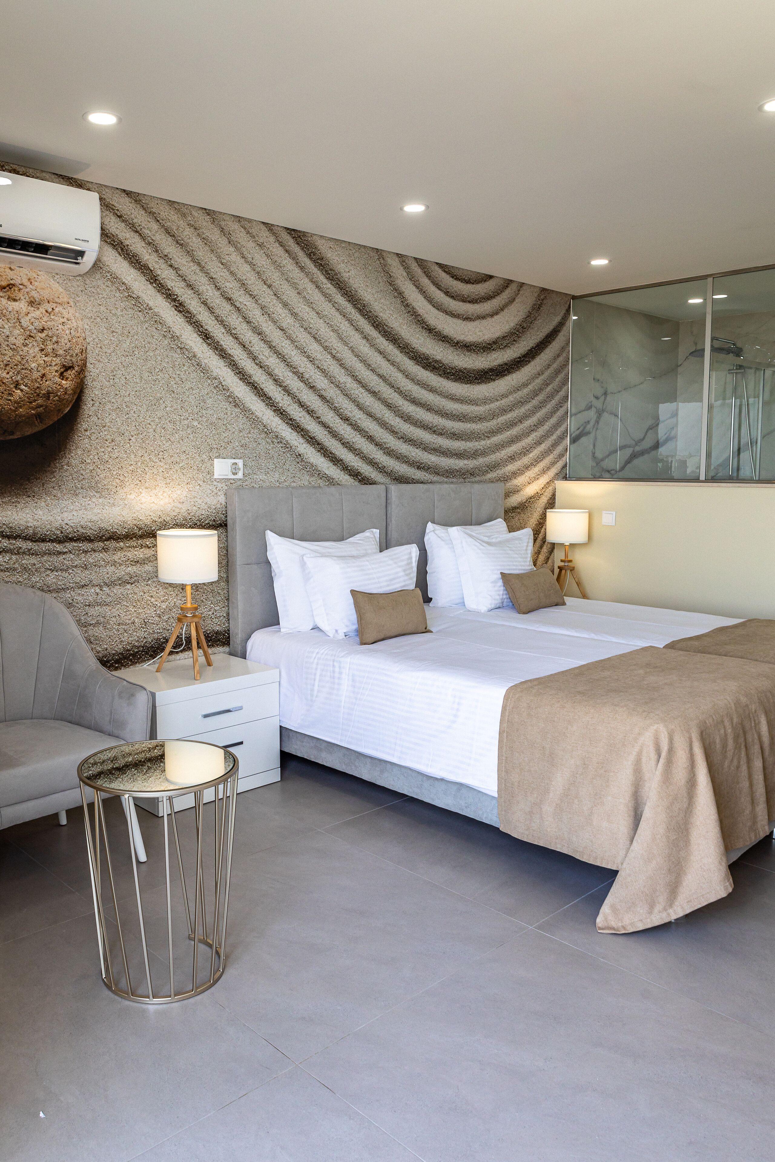 Une chambre d’hôtel moderne dotée d’un grand lit, d’un coin salon avec un canapé, d’une petite table ronde et d’un mur à texture.