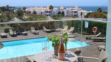 Un área de piscina en la azotea con sillones, una mesa con una botella de vino y vistas al mar y edificios al fondo.