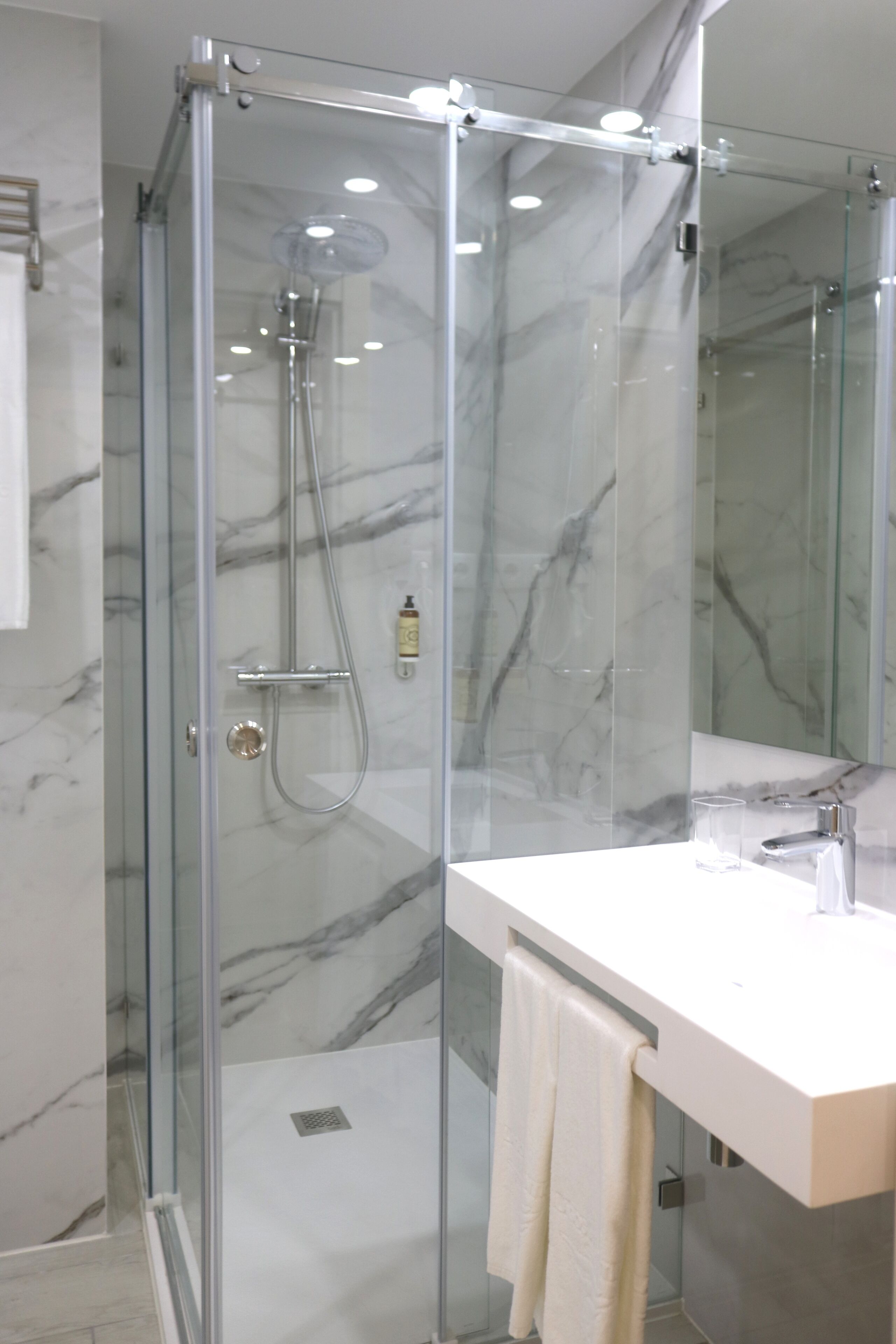 A modern bathroom with a glass-enclosed shower, a white sink, and a marble-tiled wall.