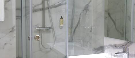 A modern bathroom with a glass-enclosed shower, a white sink, and a marble-tiled wall.