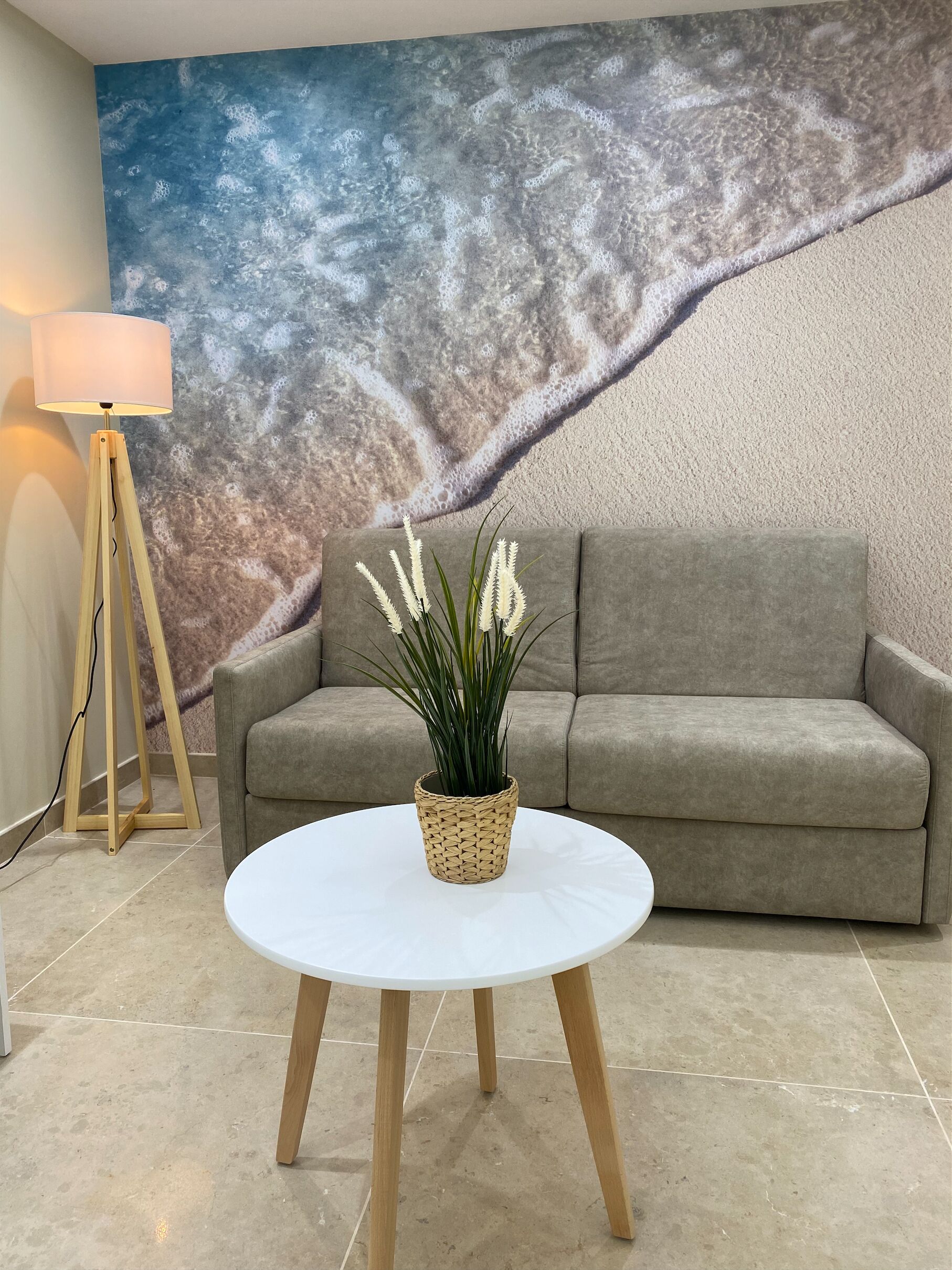 A living room with a grey sofa, a round white table with a woven plant, and a floor lamp.