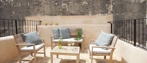 A balcony with wooden furniture, including two chairs and a table, and a pair of yellow shoes on the floor.