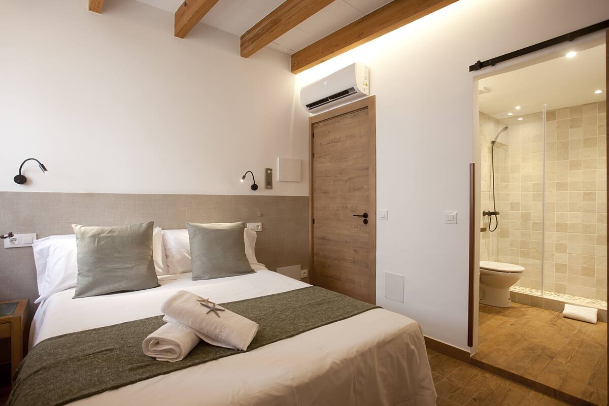 Ett hotellrum med en säng, sänglampor, en dörr av trä, en luftkonditioneringsanläggning och en duschhörna.