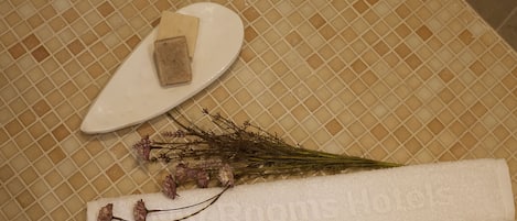 Um banheiro com piso ladrilhado, uma toalha branca e um sabonete.