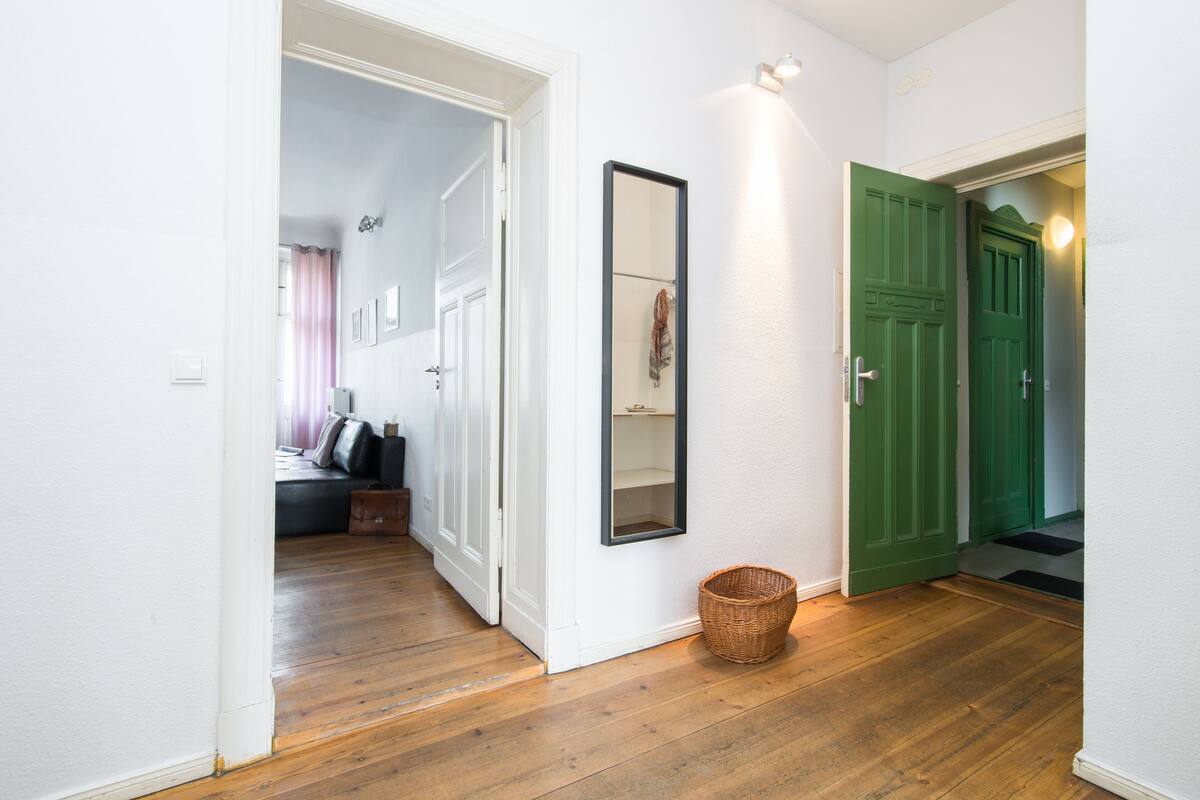 Ein Flur mit Holzboden, einer grünen Tür, einer weißen Wand und einem Spiegel.