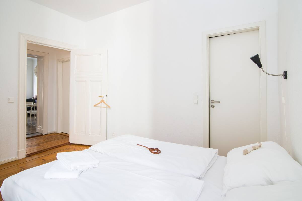 Ein Schlafzimmer mit einem Bett, einer Tür, einem Kleiderhaken und einem Flur, der in einen anderen Raum führt.