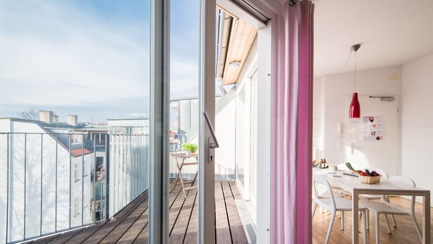 A balcony with a wooden floor, a dining area with a table and chairs, and a view of buildings in the background. - Apartments elPilar Friedrichshain (Berlin)