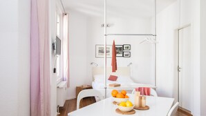 A modern, minimalist room with a white table set with fruits and a bowl, a bed with a red towel, and a white chair. - Apartments elPilar Friedrichshain (Berlin)