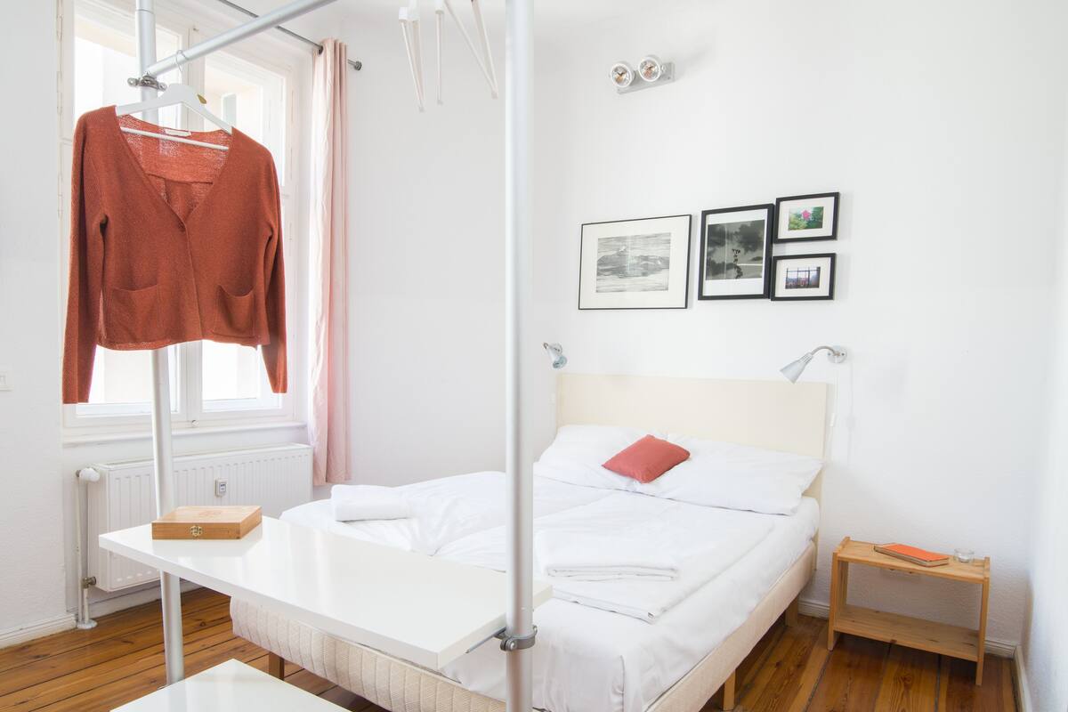 Ein ordentlich eingerichtetes Hotelzimmer mit Bett, Nachttisch, Kleiderschrank und einem Fenster mit Vorhängen.