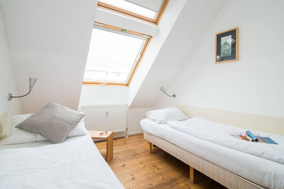 Ein kleiner, heller Raum mit zwei Betten, einem Oberlicht und einem gerahmten Bild an der Wand.