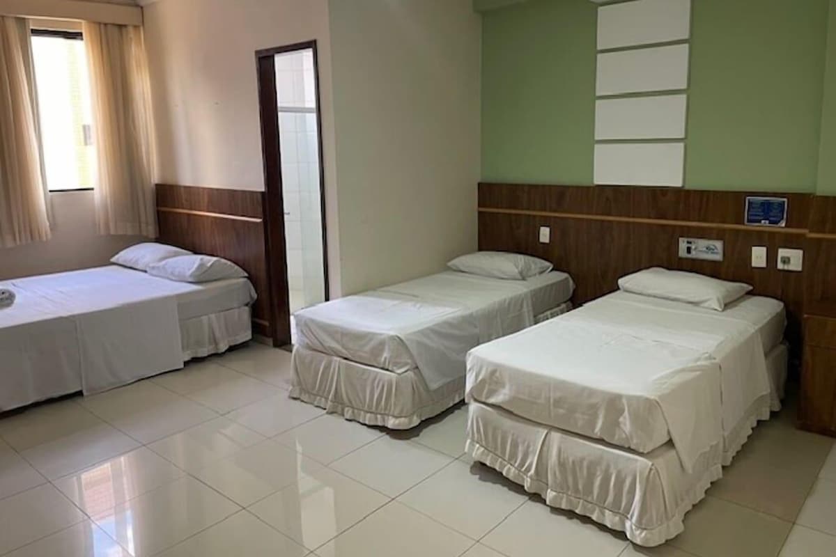 A hotel room with three single beds, a wooden headboard, a tiled floor, and a window with curtains.