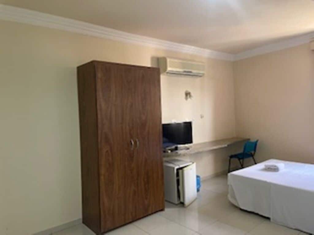 A room with a wardrobe, a bed, a desk with a computer, and a chair.