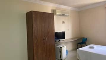 A room with a wardrobe, a bed, a desk with a computer, and a chair.