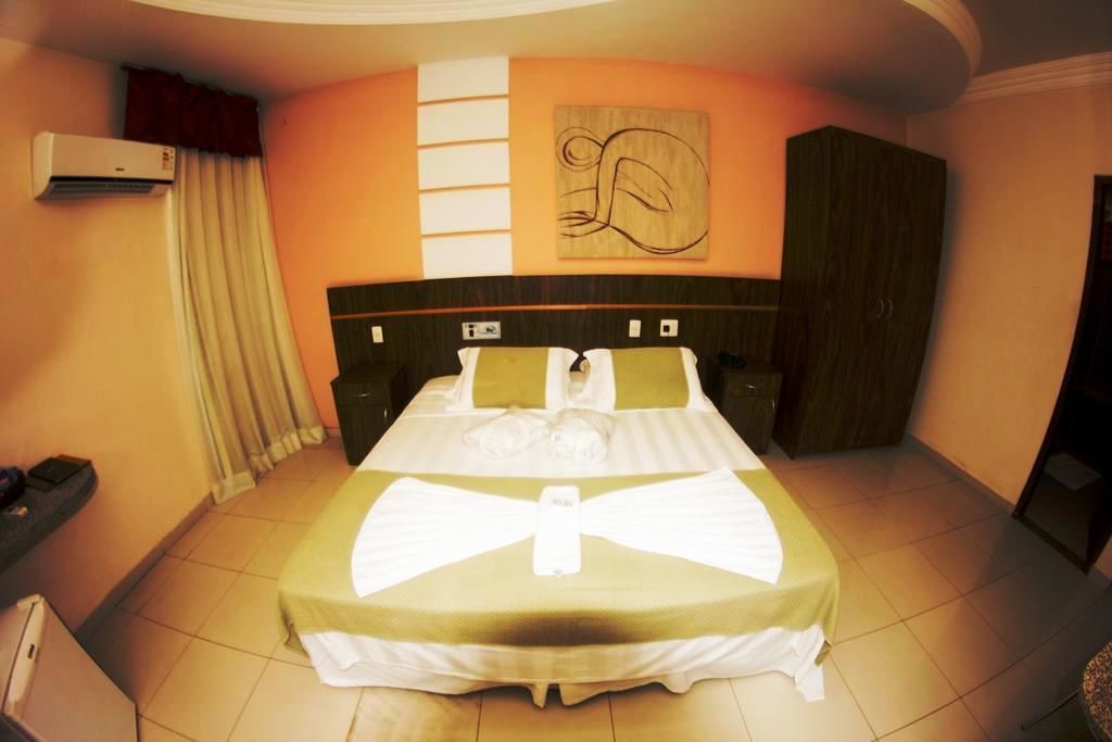 Una habitación de hotel con una cama grande, cabecera, aire acondicionado de pared y cortina.