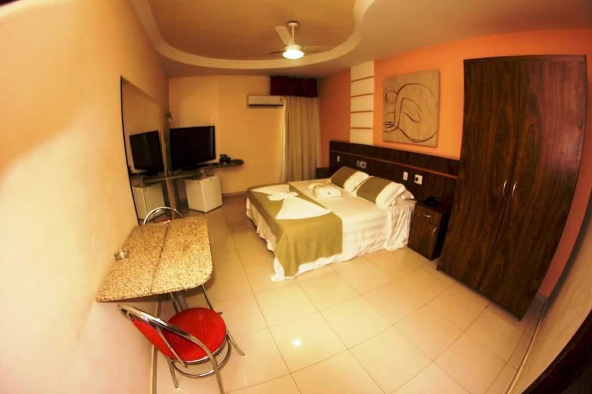 A hotel room with a bed, a desk, a chair, a TV, and a wardrobe.