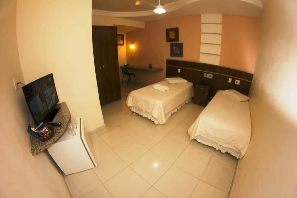 A hotel room with two beds, a desk, a television, and a small refrigerator.