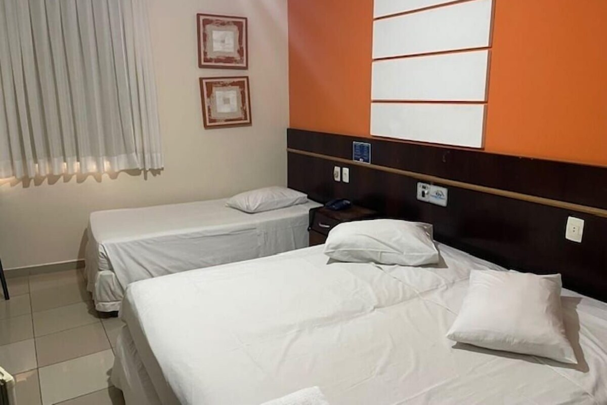 A hotel room with two beds, a window with curtains, and a wall with framed pictures.