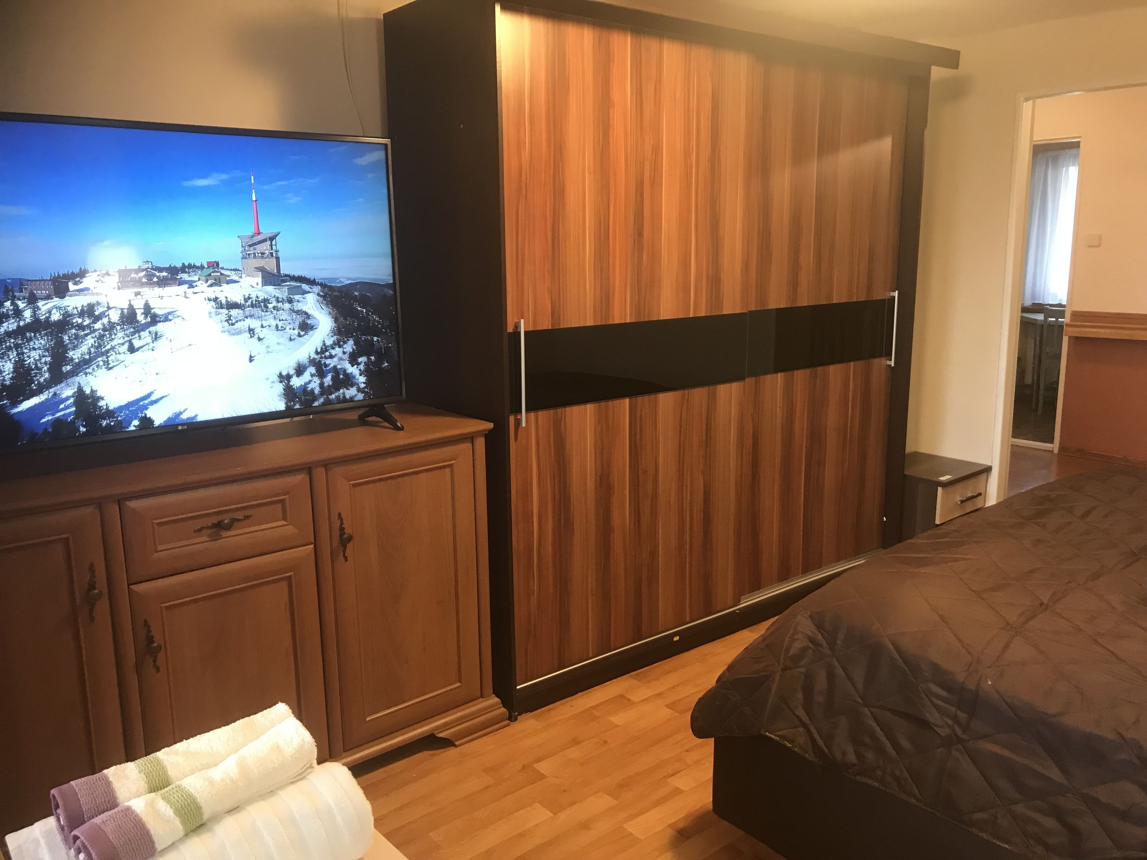 A bedroom with a bed, a television on a wooden cabinet, and a wooden wardrobe.