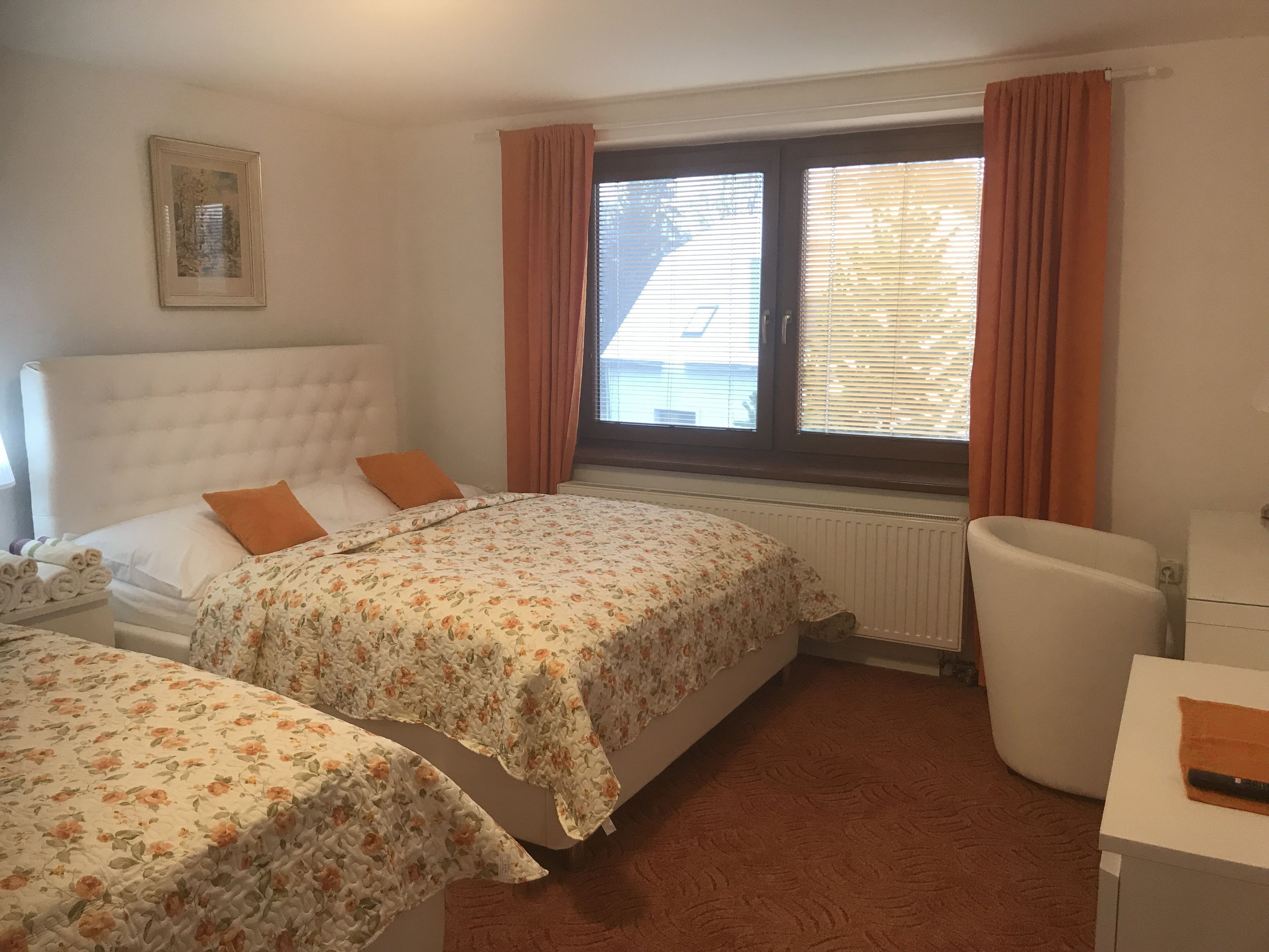 Un dormitorio con dos camas, un radiador, una ventana con cortinas, una mesita de noche y una silla.