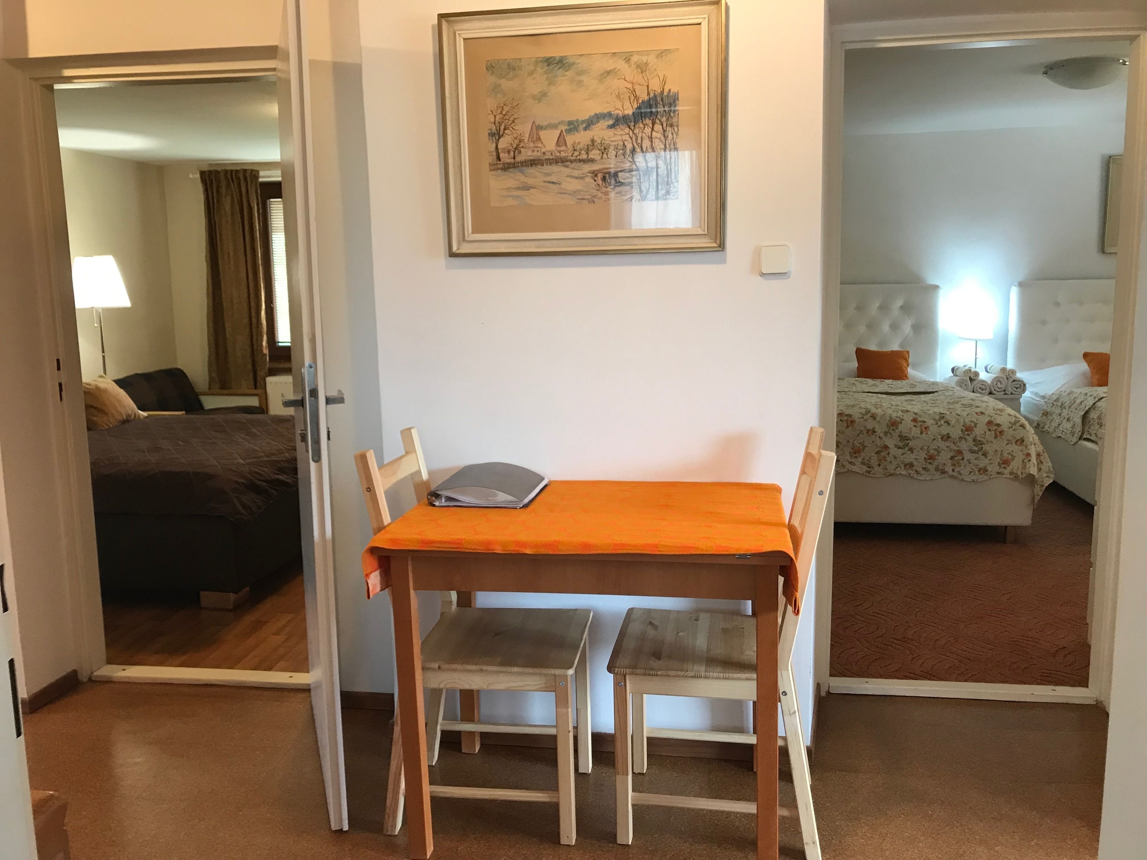 A hotel room with a bed, a desk with a chair, a framed picture on the wall, and a carpeted floor.