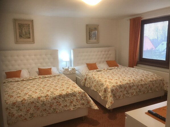 A hotel room with two beds, each with floral bedding and orange pillows, a nightstand with a lamp, and framed pictures on the walls. - Apartment pod Lysou 3 Bedroom (Frydlant nad Ostravici)