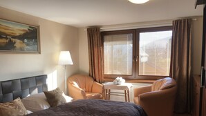 Habitació d'hotel amb un llit gran, dues butaques, una taula petita amb tovalloles, un quadre a la paret i una finestra amb cortines.