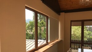 Habitació amb una finestra gran, sostre de fusta i vista a arbres i muntanyes.