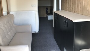 Habitació amb un sofà blanc, un moble negre amb taulell blanc, un radiador i una paret de fusta.